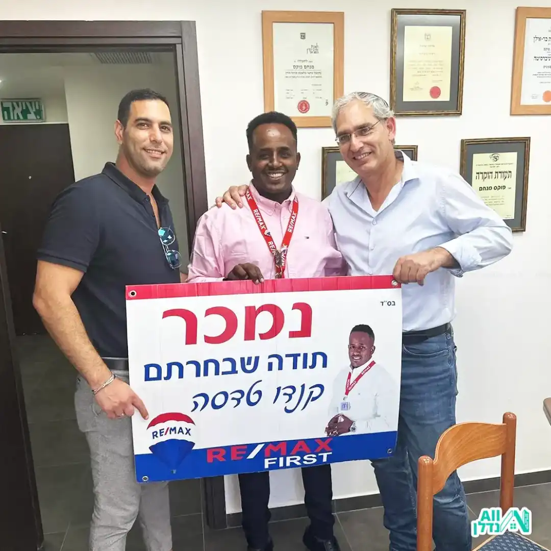 שני גברים מצטלמים אחד מחזיק שלט "נמכר" והשני מחזיק מתנה